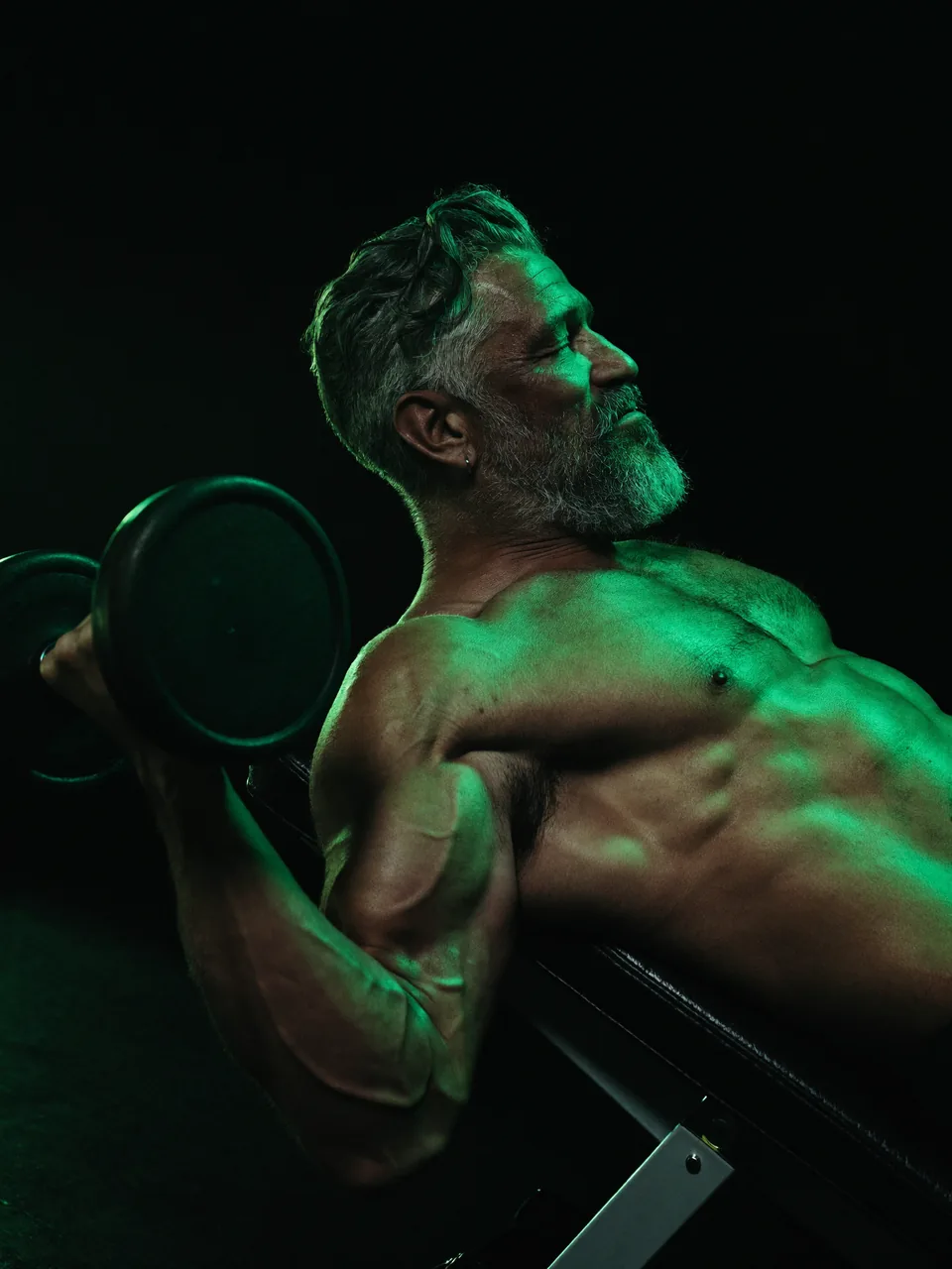 A man in his sixties training with a dumbbell in a dark gym