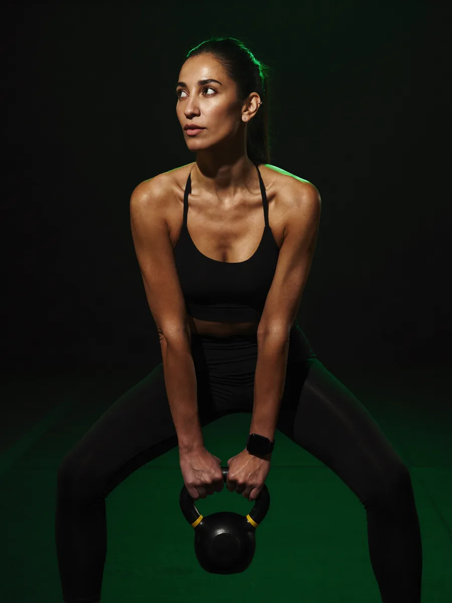 A young woman holding a kettlebell in a dark gym